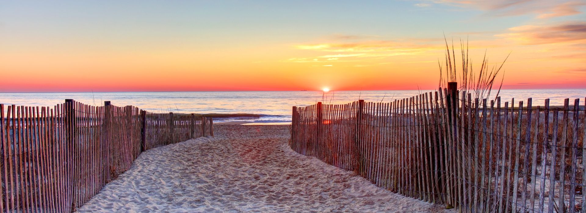 Sandy path out to the ocean during a brillian red and orange sunset