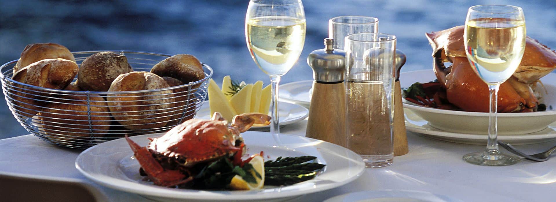 Waterfront dining table with white linen cloth and plates, fresh seafood, and chilled white wine