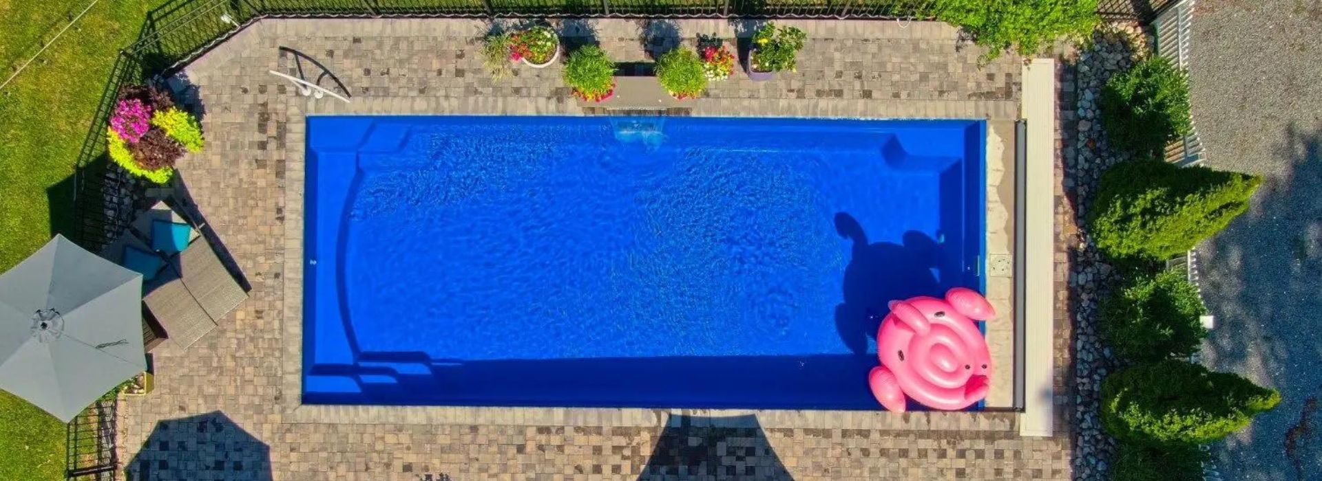 Aerial view of deep blue rectangular inground swimming pool surrounded by a stone deck with plants and furniture