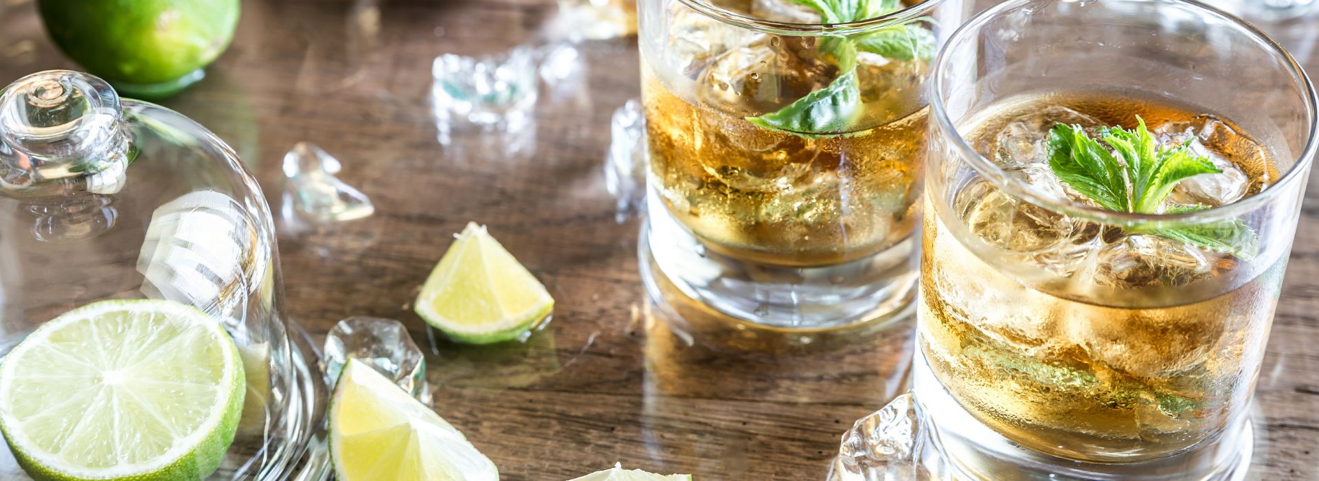 Two iced glasses of rum drinks with herbs and lime wedges