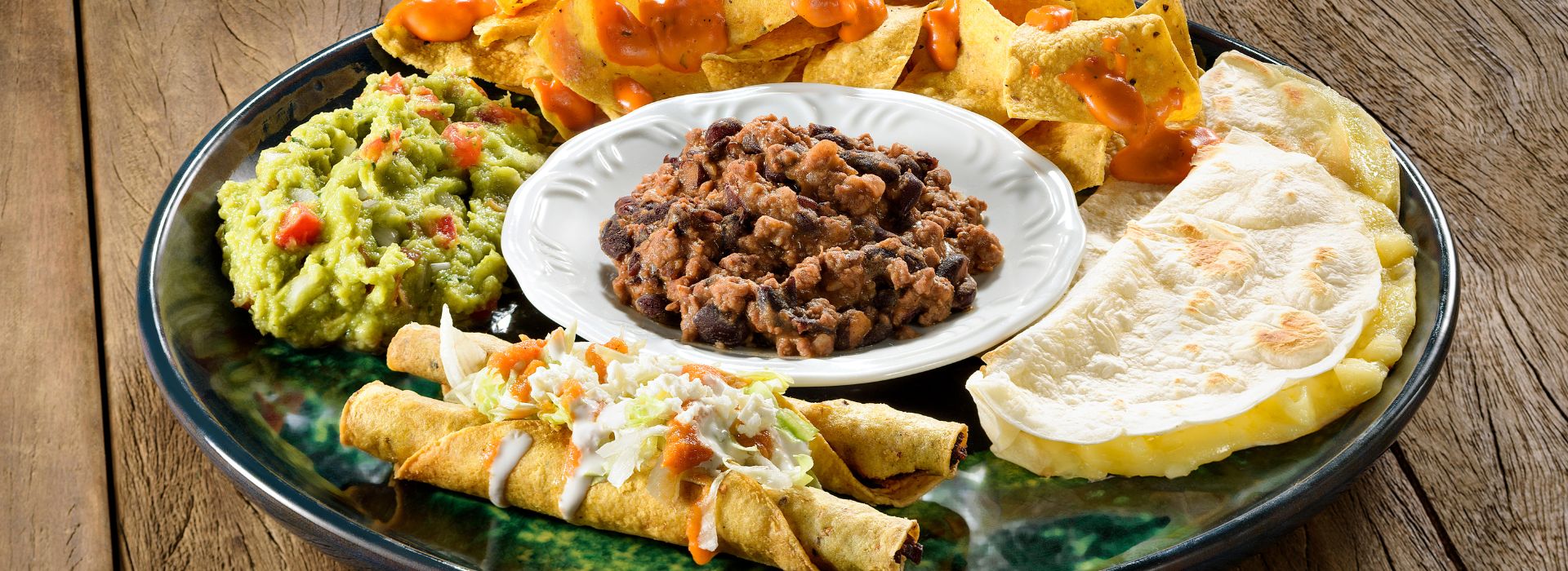 a blue plate filled with tex-mex including tostitos, refried beans, quesadillas, tortilla chips, and guacamole