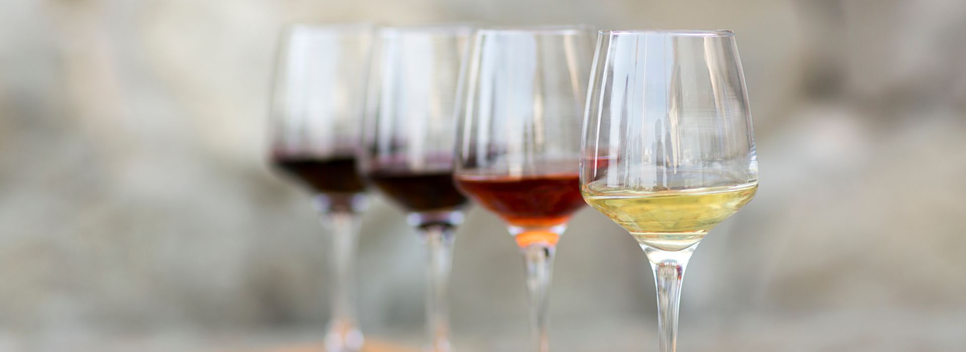 Four wine glasses partially filled with white, red and burgundy colored wines
