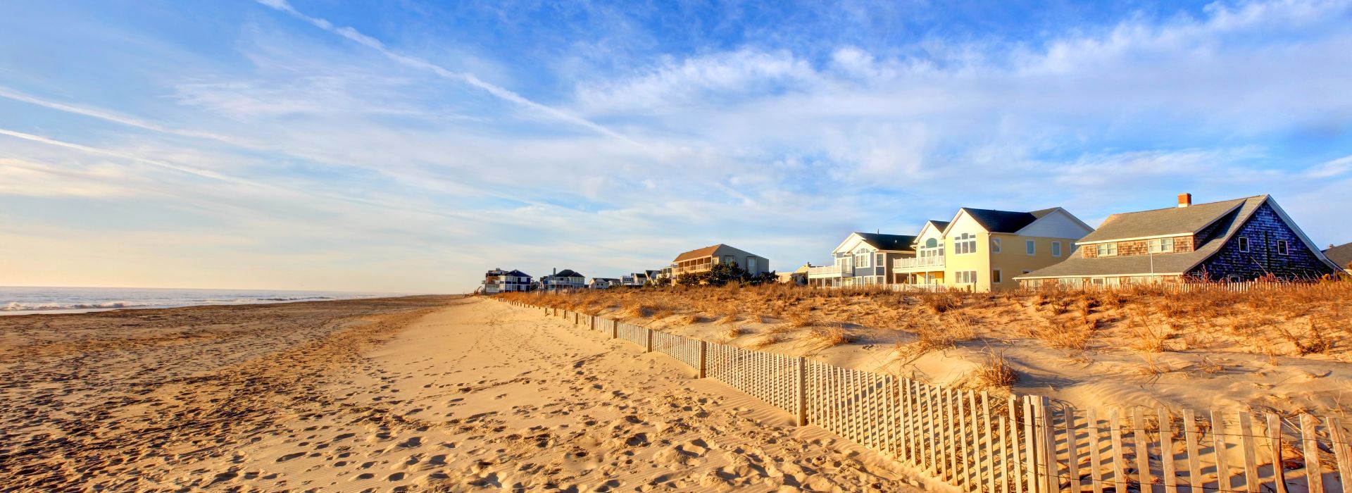 Sandy Dewey Beach on a summer day with blue skies, soft clouds, and nearby beach houses.