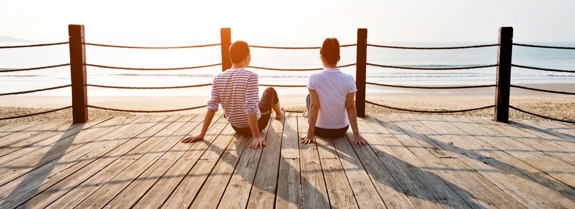 A couple is sitting on a boardwalk overlooking the water
