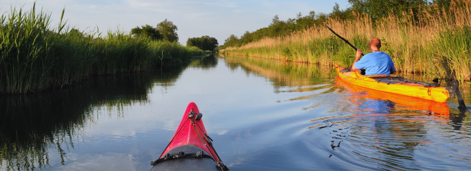 two people kayaking on a river lined with marsh plants